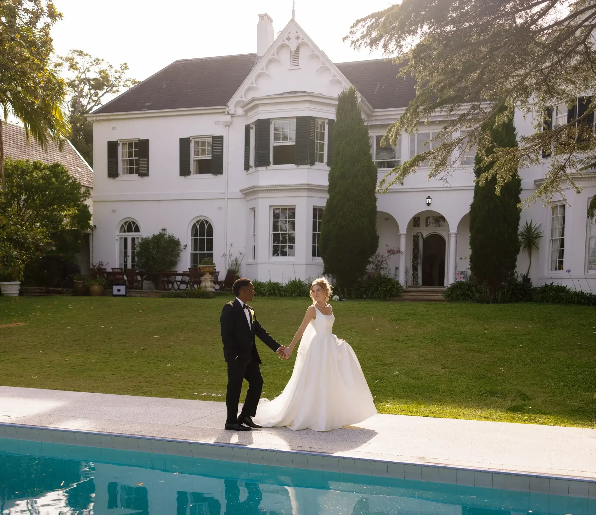 Couple holding hands by elegant white mansion with swimming pool