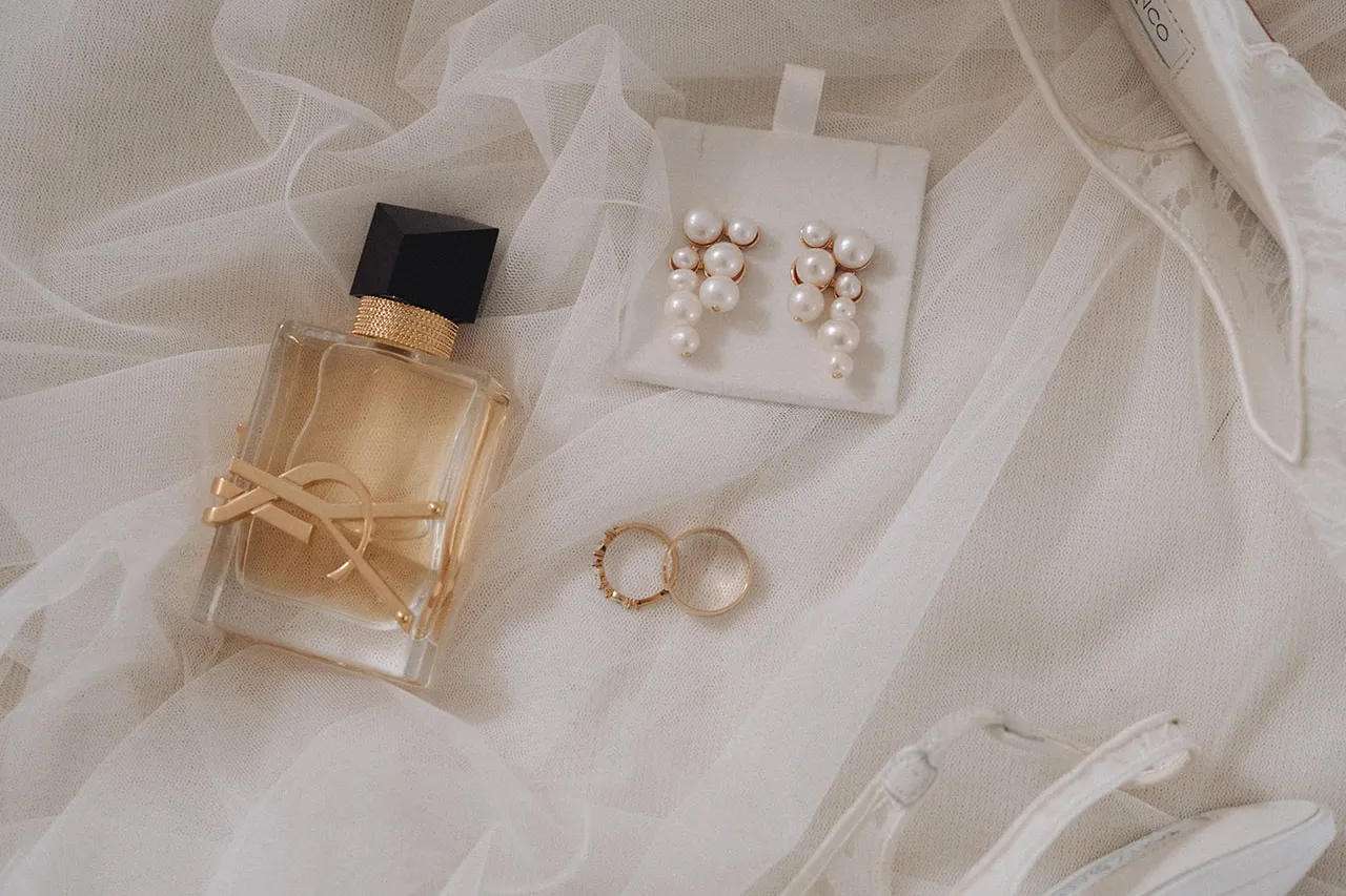Flat lay of wedding rings, pearl earrings, perfume and bridal heels