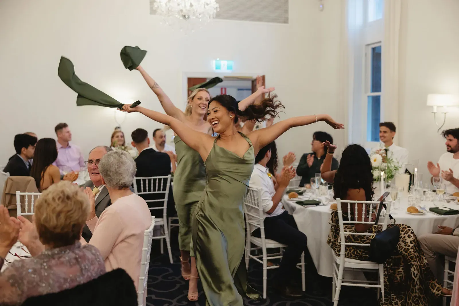Bridal party dancing into a reception, twirling napkins as guests cheer
