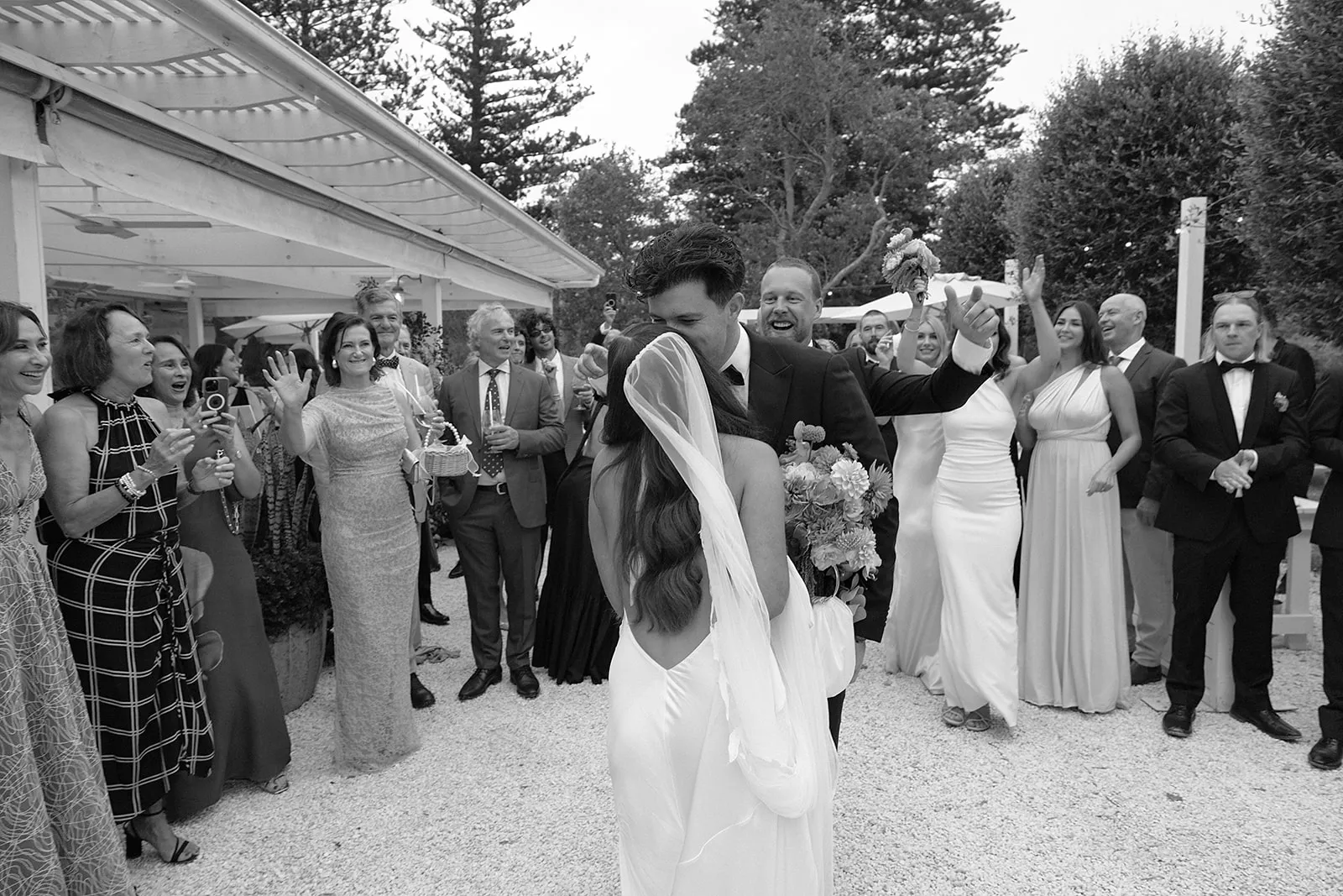 Black and white photo of guests cheering as a couple leaves their ceremony