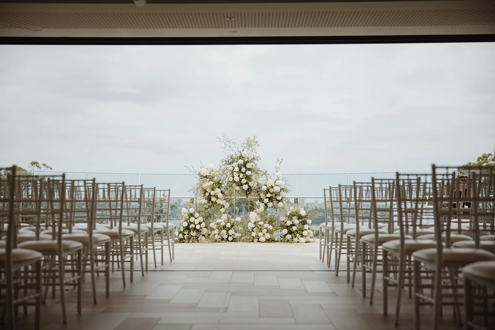 Empty ceremony aisle with a white floral arch and Sydney Harbour behind
