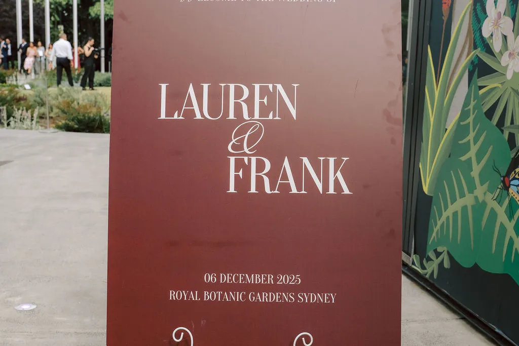 Burgundy wedding welcome sign on a white easel outside a garden venue